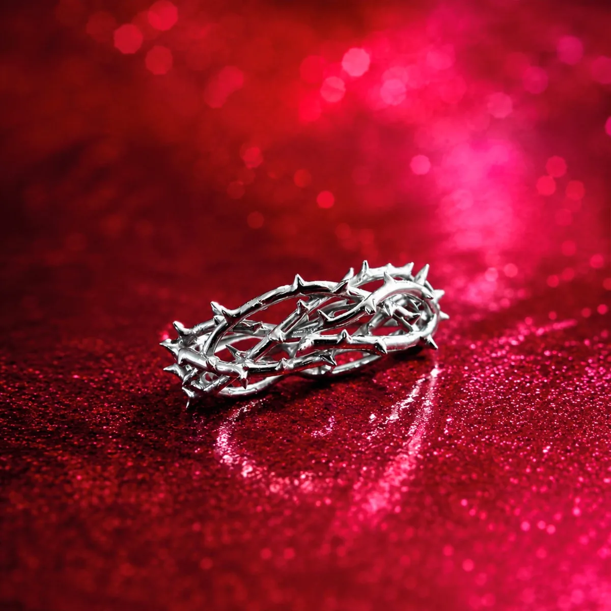 Anillo DOPA de plata con forma de corona de espinas sobre un fondo de brillo rojo y fucsia