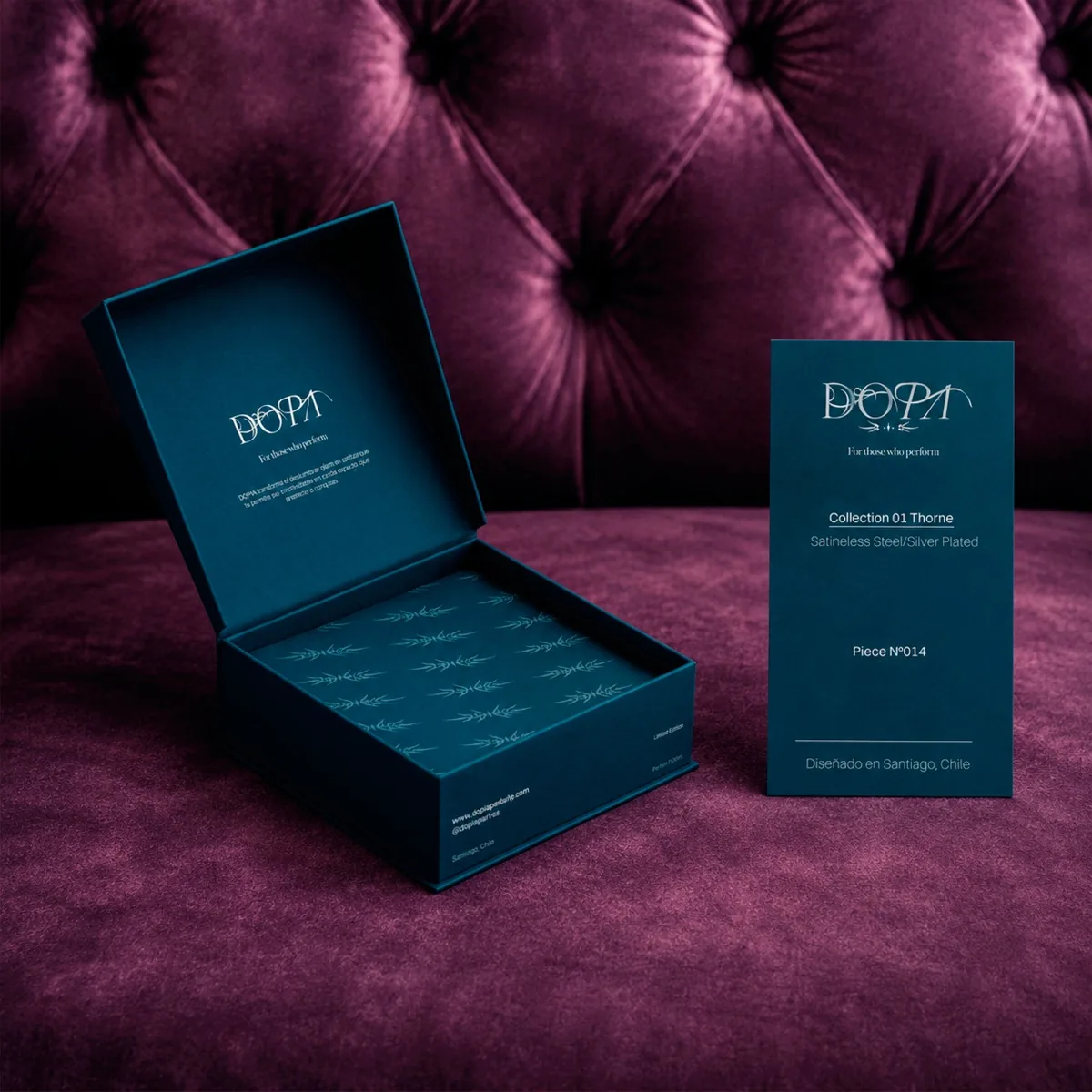 Packaging DOPA: caja azul petróleo abierta con el logotipo y una tarjeta de la Collection 01 Thorne, sobre un sillón capitoné de terciopelo morado