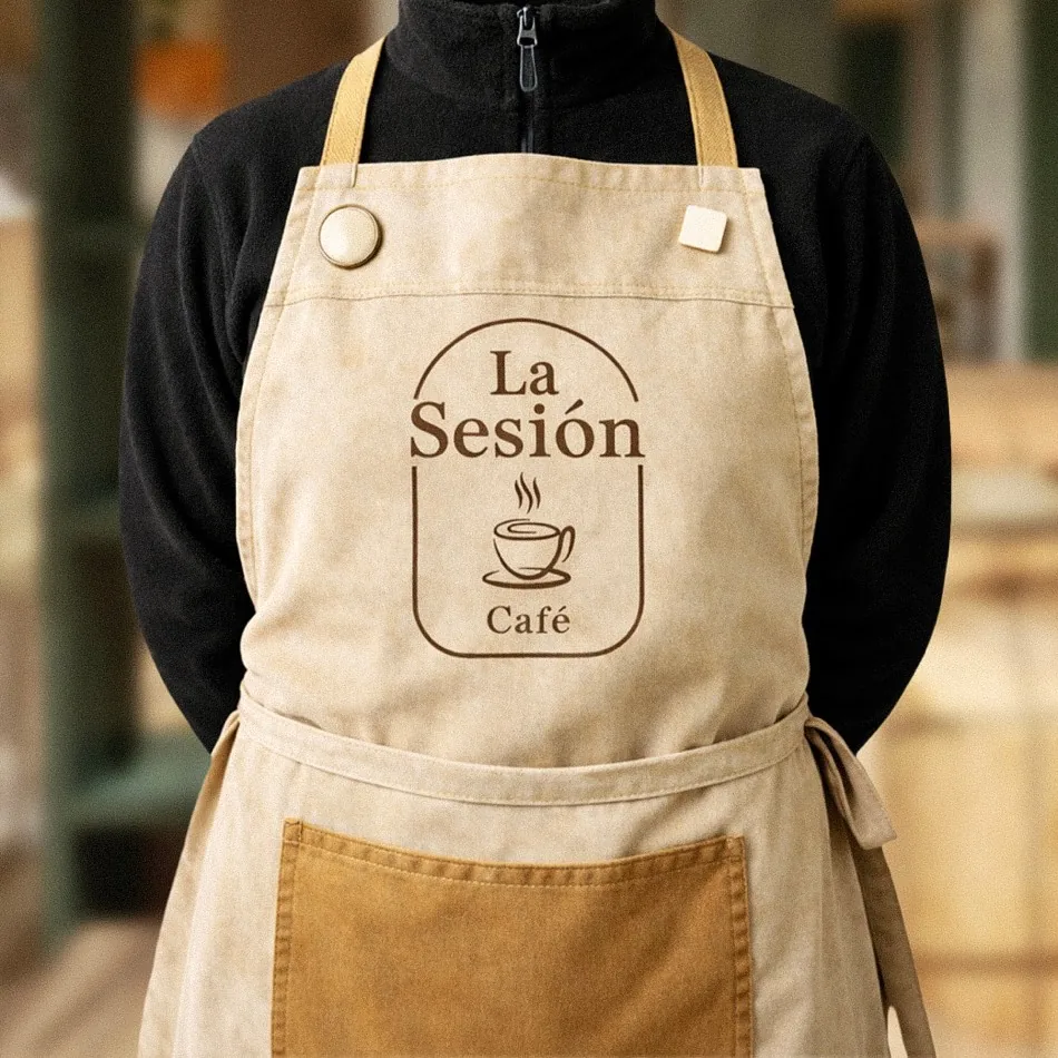 Delantal de lino crema con el logotipo de La Sesión Café en arco, una taza y la palabra Café
