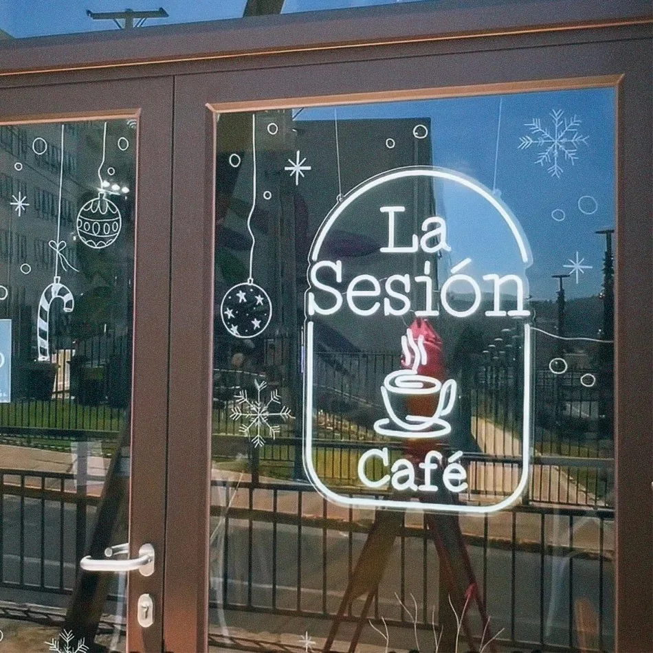 Logotipo de La Sesión Café en neón blanco tras la vidriera del local, decorada con copos de nieve y adornos navideños